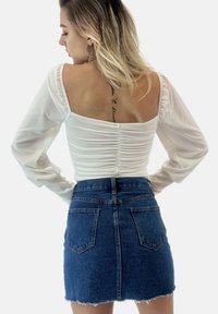 Maglietta bianca a maniche lunghe con dettaglio arricciato sul retro, abbinata a una gonna di jeans blu scuro a vita alta con orlo sfilacciato e due tasche posteriori.