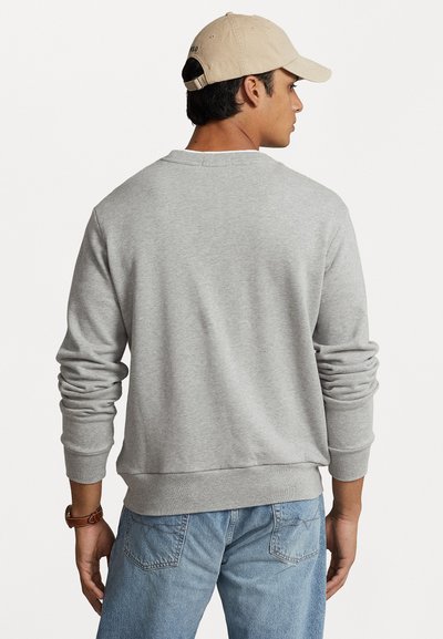 Svijetlosiva dukserica od mekanog materijala s dugim rukavima i rebrastim manžetama. Kombinirana sa svijetlop Plavim trapericama, viđena s leđa.