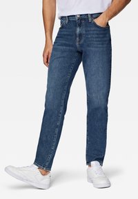 Jeans de mezclilla azul oscuro con un corte recto. Presentan un diseño clásico de cinco bolsillos, presillas para cinturón y detalles de decoloración sutil. Combinados con zapatillas blancas.