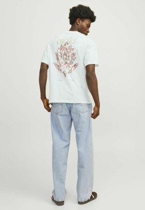 Lichtblauwe katoenen t-shirt met een grafisch ontwerp van een bloem op de achterkant, gecombineerd met blauwe spijkerbroeken en bruine sandalen.