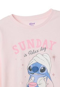 Camiseta rosa claro con Stitch de Disney. El texto dice "DOMINGO es día de relajación". Material de algodón suave con acentos de estrellas brillantes.