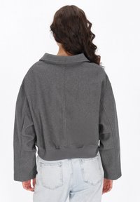 Grå kort jacka med bred krage, i en texturerad tyg med vida ärmar. Matchas med ljusblå jeans.