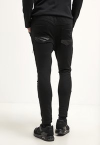 Černé tepláky s quiltovaným pasem, texturovanými kapsami a slim fit střihem. Spárované s černými sportovními botami. Hladký materiál, ležérní design.