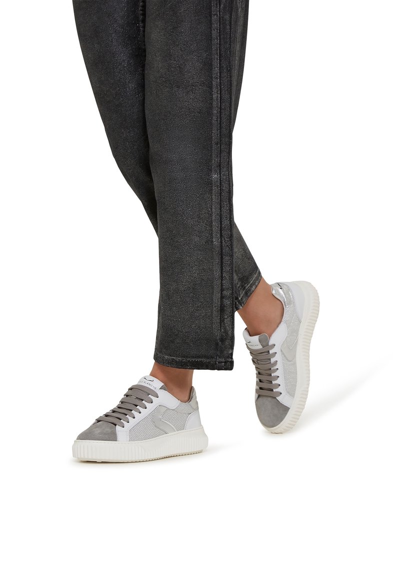 Baskets grises et blanches avec un dessus en maille texturée et des accents en daim, dotées d'une semelle en caoutchouc et de lacets plats, associées à un pantalon noir fuselé.