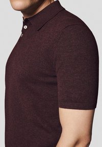 Burgundowa koszulka polo z krótkim rękawem, wykonana z dzianiny, z klasycznym kołnierzykiem i zapięciem na trzy guziki, o gładkiej teksturze.