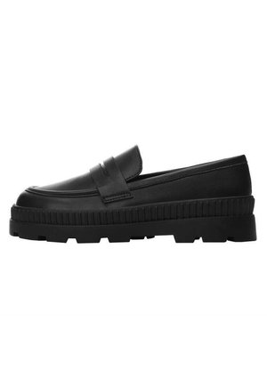 Mocassin en cuir noir avec une semelle épaisse à rainures et une bride décorative sur le dessus, présenté en profil latéral sur fond blanc.