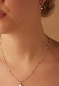 Zilveren ketting met een klein kruisjeshanger; bijpassende zilveren oorbellen met een hoop en hangende kruisjes; soepele textuur, minimalistisch ontwerp.
