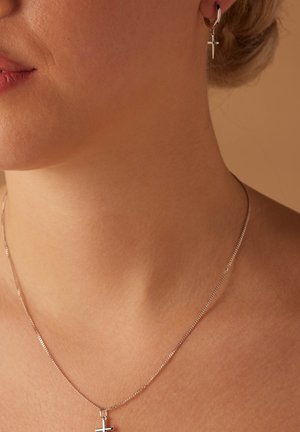 Collier en argent avec un petit pendentif croix ; boucles d'oreilles en argent assorties avec des charms croix pendants ; texture lisse, design minimaliste.