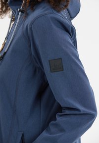 Laivaston sininen kevyt takki, jossa on teksturoitu pinta, säädettävä kiristysnauha hupussa ja musta logopatchi hihassa.