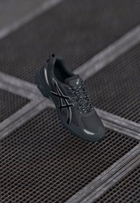 Dark gray athletic shoe featuring a textured upper, reflective accents, and a durable rubber sole with a distinct tread pattern.