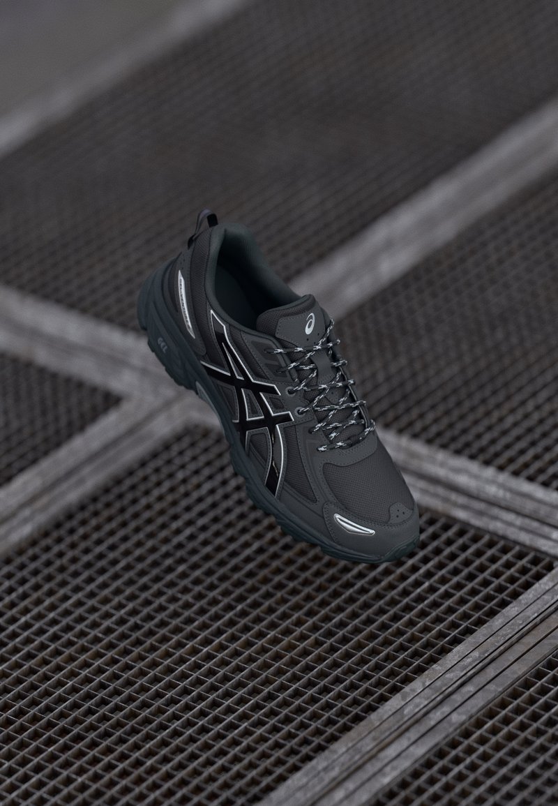 Dark gray athletic shoe featuring a textured upper, reflective accents, and a durable rubber sole with a distinct tread pattern.