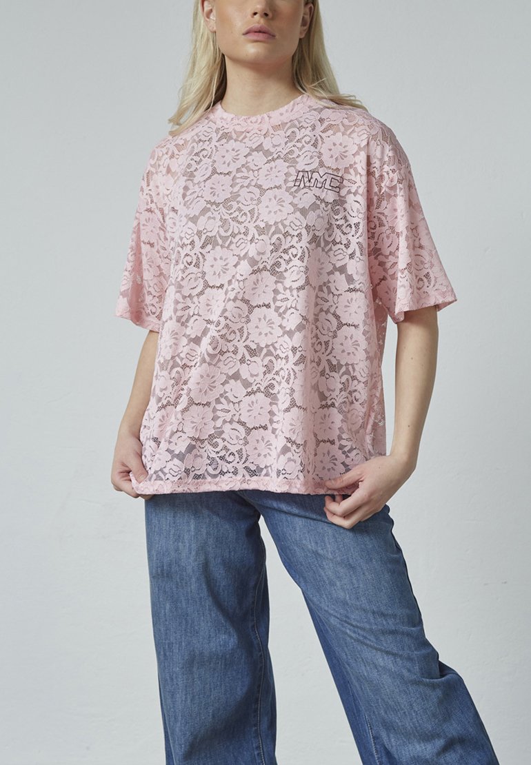 Lyserød blonde t-shirt med blomstermønster, korte ærmer og rund hals. Har logo-detail på brystet. Løs pasform, parret med blå jeans.