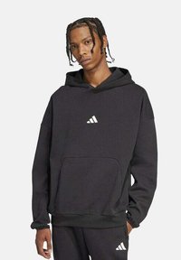 Sudadera negra hecha de un material suave que cuenta con un bolsillo frontal, puños acanalados y un pequeño logotipo triangular blanco en el pecho.