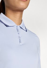 Light blue polo shirt with a collared neckline, featuring a navy accent, concealed button placket, and smooth fabric texture.