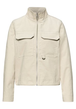 Veste beige en velours côtelé avec col montant, fermeture éclair devant, deux poches poitrine à rabat et un petit détail en anneau métallique sur la poche droite.