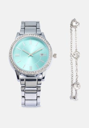 Silver metal watch with an aqua dial, crystal-studded bezel, and date display. Includes a matching silver chain bracelet with two clear stones.