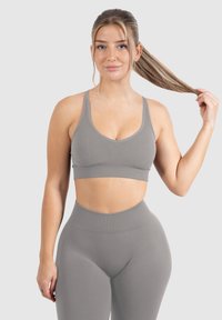 Un sujetador deportivo gris y leggings de cintura alta a juego presentan un diseño sin costuras, una tela suave y una silueta ajustada.