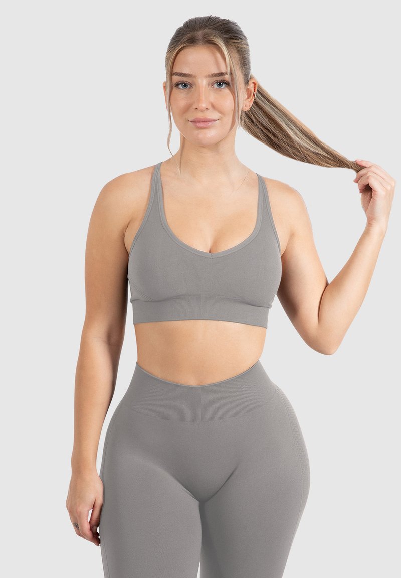 Un sujetador deportivo gris y leggings de cintura alta a juego presentan un diseño sin costuras, una tela suave y una silueta ajustada.