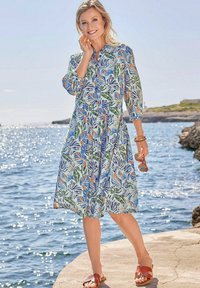 Blumenmusterkleid aus leichtem Stoff, mit 3/4-Ärmeln, einer Knopfleiste und einem schwingenden Saum. Die Farben umfassen Grün, Blau, Orange und Weiß.