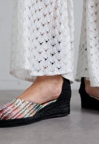 Pantofi cu toc wedge din material țesut multicolor, cu o talpă și platformă din iută neagră, asortați cu pantaloni largi, texturați, albi.
