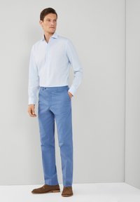 Svijetloplava košulja dugih rukava s dugim rukavima, u kombinaciji s krojenim svijetloplavim hlačama i smešnim cipelama. Glatka tkanina, slim-fit dizajn.