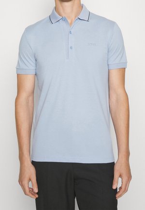 Homme portant un polo à manches courtes bleu clair avec col boutonné et logo "BOSS" sur la poitrine, associé à un pantalon noir.
