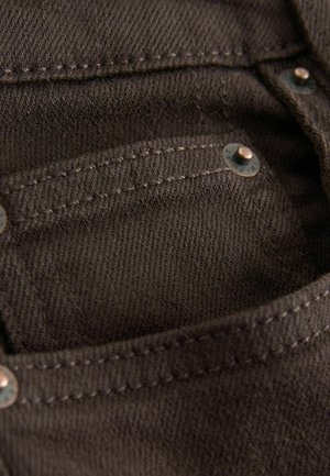 Brown denim fabric close-up showing pocket detail, visible stitching, and metal hardware accents in a slightly textured finish.