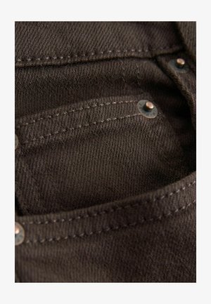Brown denim fabric close-up showing pocket detail, visible stitching, and metal hardware accents in a slightly textured finish.