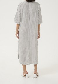 Robe en lin rayée à manches courtes, avec une coupe droite, des fentes latérales et un col arrondi. Portée avec des chaussures blanches à talons blocs.