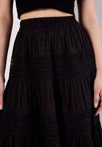 Gonna nera a più livelli con una vita testurizzata e accenti in crochet orizzontali. Realizzata in tessuto leggero con un design fluido.