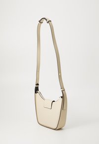 Sac à épaule en cuir beige avec un design courbé, un bord contrastant foncé, une sangle réglable et un rabat à fermeture en haut.