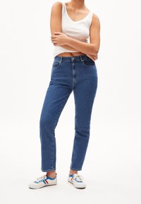 Höga blå denimjeans med rak passform, fem fickor och en blekt textur. Parat med en vit linne och sneakers med blå detaljer.