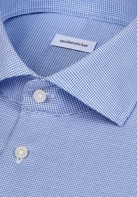 Chemise bleu clair à petit motif à carreaux, col plié, deux boutons blancs, et étiquette de marque Seidensticker visible à l'intérieur du col.