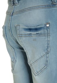Svetle modré džíny mají klasický design se pěti kapsami, vyztuženým švem a výraznou zadní kapsou s jemným detailem loga.