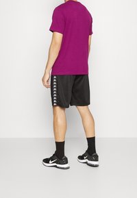 Fuchsie tričko s krátkým rukávem spárované s černými šortkami s bílým bočním potiskem; nošeno s černými teniskami a kotníkovými ponožkami.