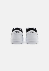Baskets Vans blanches avec un col noir, cuir texturé et semelle en caoutchouc. Présente un logo sur le talon et un design simple et épuré.