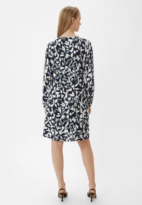 Kleid mit langen Ärmeln, schwarz-weißem abstraktem Muster, tailliert, knielang, aus leichtem Stoff, kombiniert mit schwarzen High Heels.