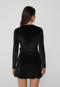 Czarna aksamitna sukienka z długimi rękawami, dopasowanym gorsetem i rozkloszowaną spódnicą; posiada fakturowany wzór oraz pasek do wiązania w talii.