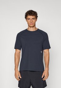 Navy blue athletic t-shirt with short sleeves, round neckline, seamless shoulder design, and a small logo on the bottom right.