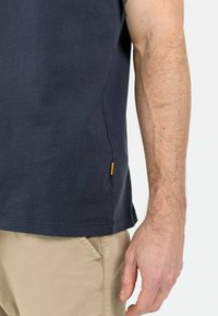 Marineblå bomulds T-shirt med korte ærmer, med et sidesømsetikette i lys orange, som viser en afslappet pasform og blød tekstur.