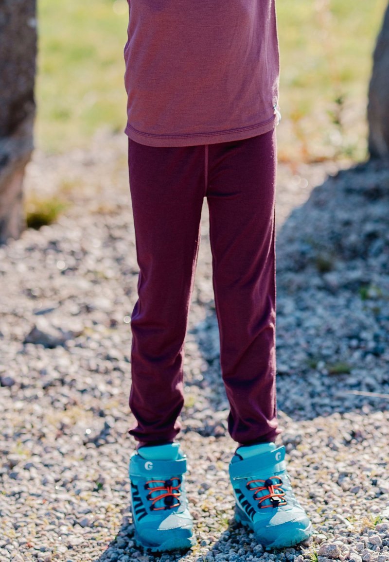 Bordeaux leggings lavet af strækbart stof, parret med turkise og sorte sko med klare orange snørebånd, på en grusoverflade.