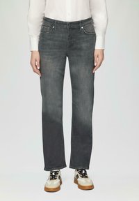 Jean en denim gris avec une coupe droite, cinq poches et une légère décoloration. Associé à une chemise blanche et des chaussures beiges avec des lacets noirs.