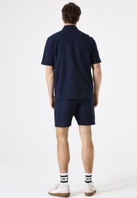 Marineblauw polo met korte mouwen en bijpassende korte broek van een gestructureerde stof, met een eenvoudig ontwerp. Gecombineerd met witte sokken en lichte sneakers.