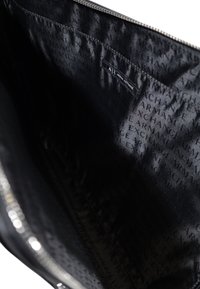Interno nero di una borsa con una texture liscia, caratterizzato da un motivo a logos ripetuti "Armani Exchange" e una chiusura con zip argentata.