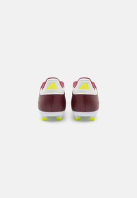 Scarpe da calcio color bordeaux con accenti bianchi e suola gialla a tacchetti. Presenta il logo Adidas e un materiale simile alla pelle liscia nella parte superiore.