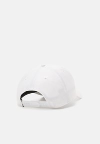Gorra de béisbol blanca con una corona redondeada, un visor plano y una correa ajustable. Presenta agujeros de ventilación y una textura suave.