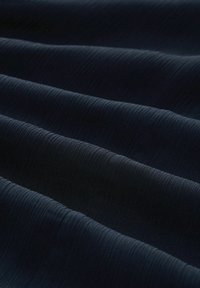 Marineblauer Stoff mit einer strukturierten Oberfläche, der leichte horizontale Linien und einen sanften Glanz aufweist, in sanften Falten gelegt.