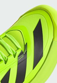 Baskets de sport vert néon avec un dessus en mesh texturé, des accents noirs et des lacets plats. La semelle présente une légère courbure pour un meilleur soutien.