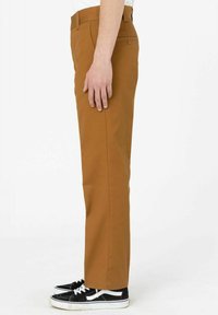 Braune, schmal zulaufende Hosen mit Seitentaschen, aus glattem Stoff. Getragen mit schwarzen Sneakers mit weißen Akzenten und Schnürsenkeln.