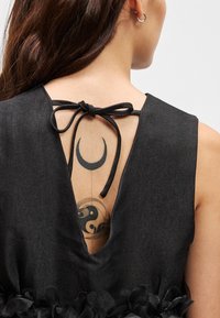 Vestido preto com um design de costas em V, apresentando um fecho de laço e uma fralda texturizada na bainha. Tatuagem visível nas costas.